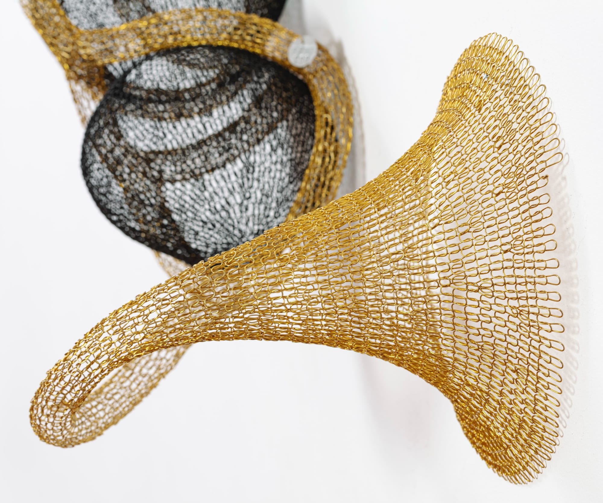 detail of a gold and black abstract woven metal sculpture with tubes and circular forms on a wall