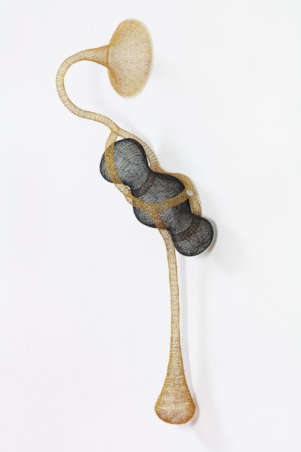 a gold and black abstract woven metal sculpture with tubes and circular forms on a wall