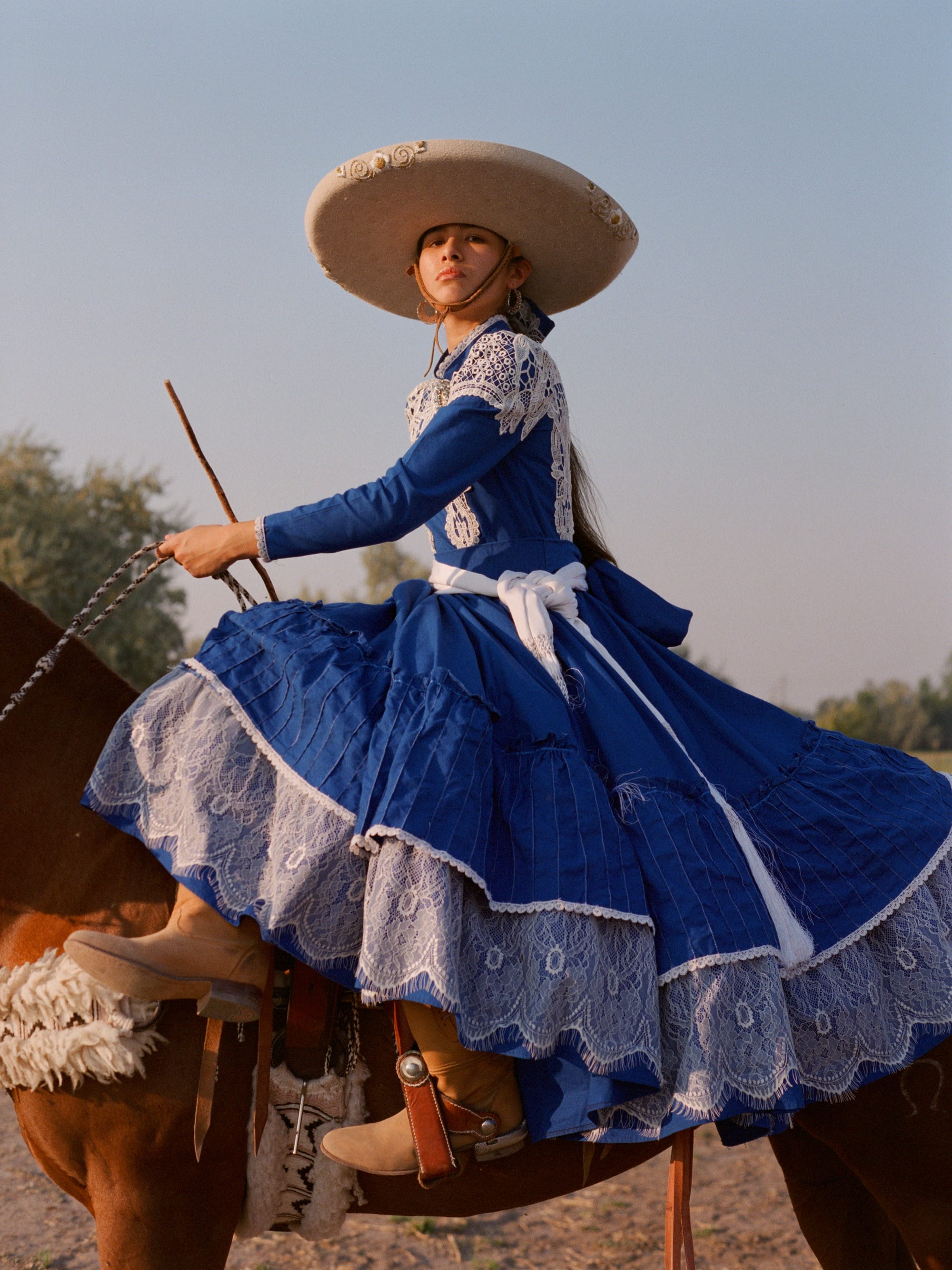 a woman on horseback wears a blue-and-white dress with a wide-brimmed hat