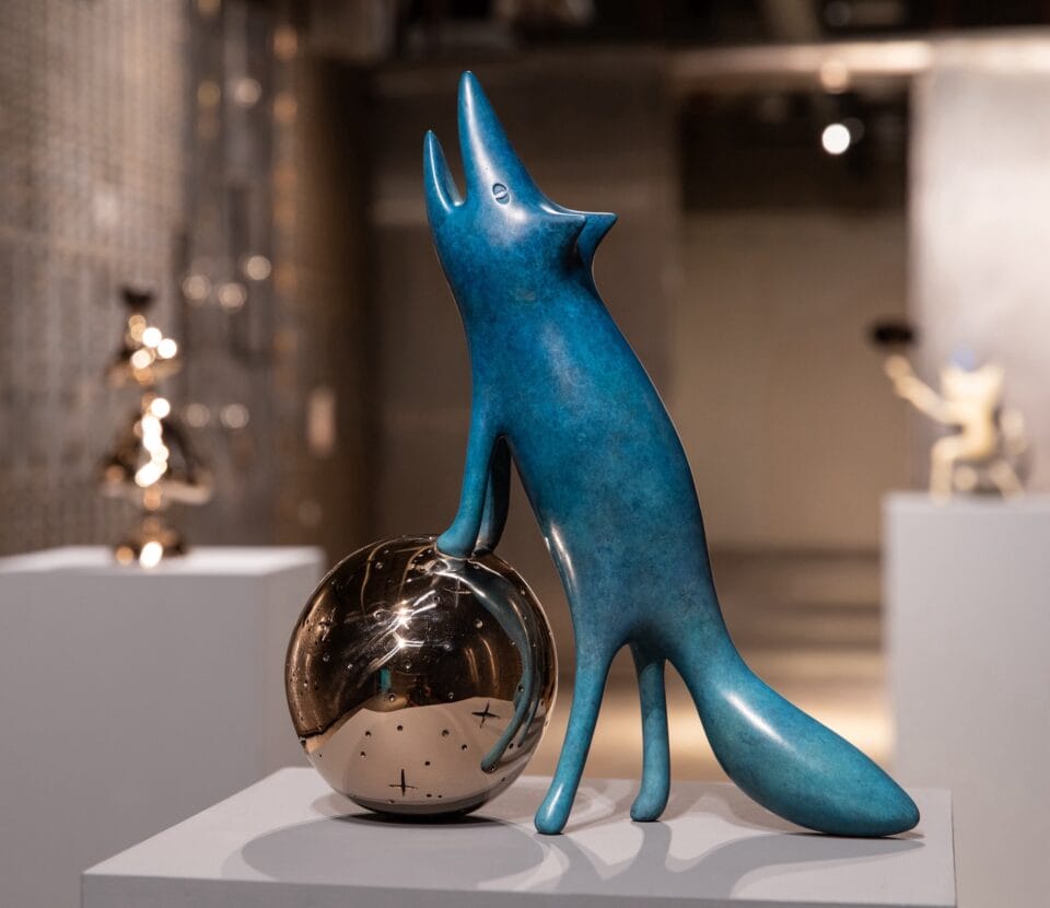 a sculpture of a cartoonish coyote or wolf, standing on a ball